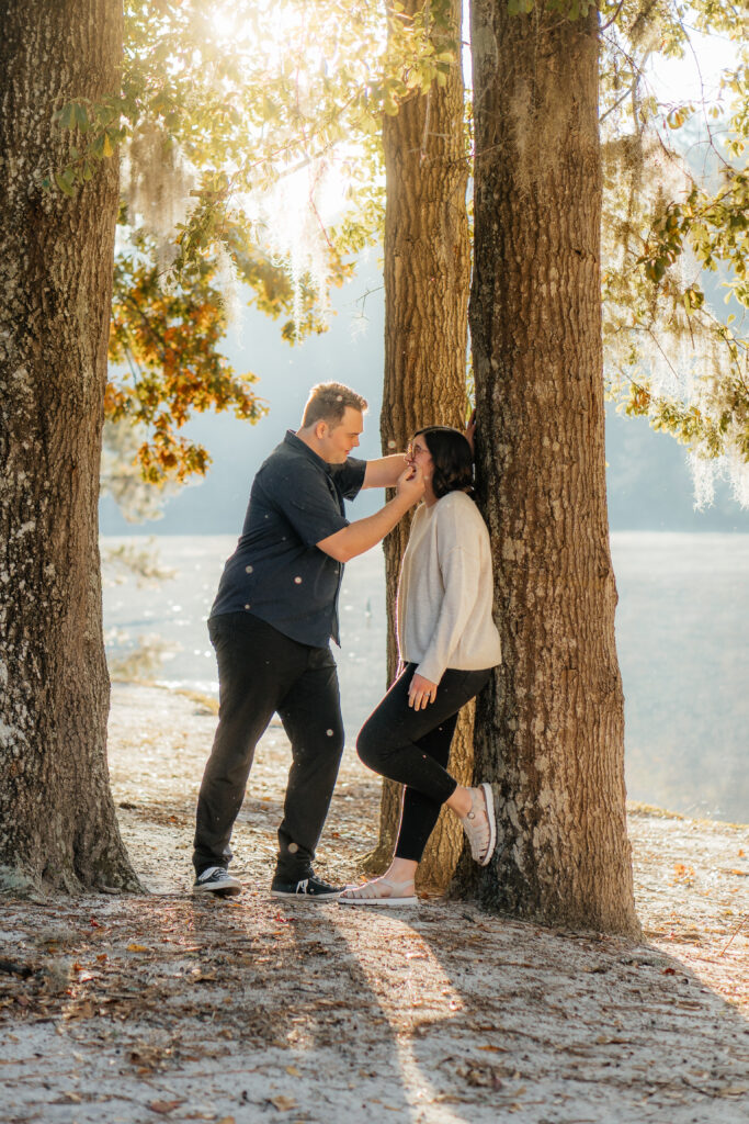 couple leaning against tree with light filtering in through spanish moss